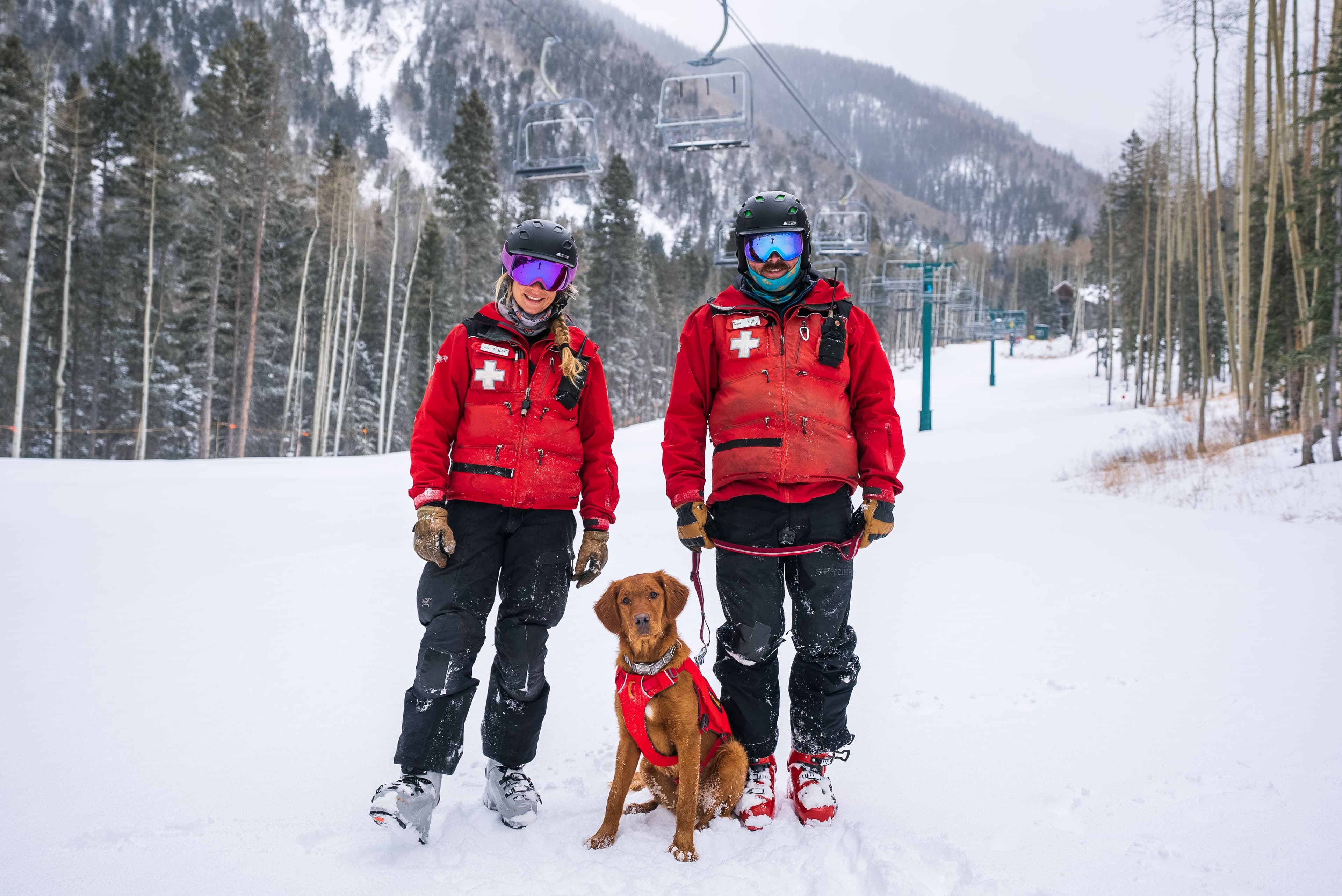 Two ski patrollers pose with a patrol dog