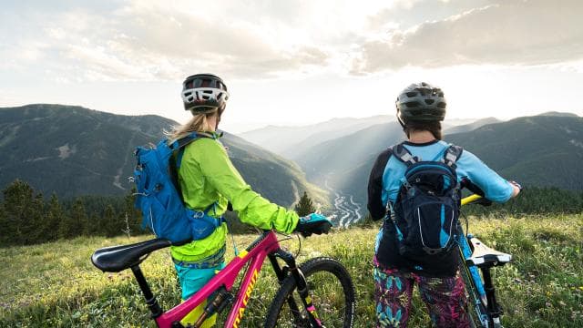 Two mountain bikers pause on a grassy ridgeline in Taos Ski Valley and watch the sunset.