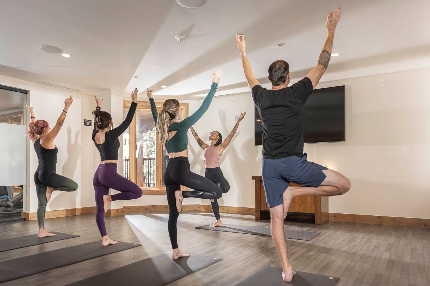 A group of four people hold tree pose in a yoga class at The Blake.