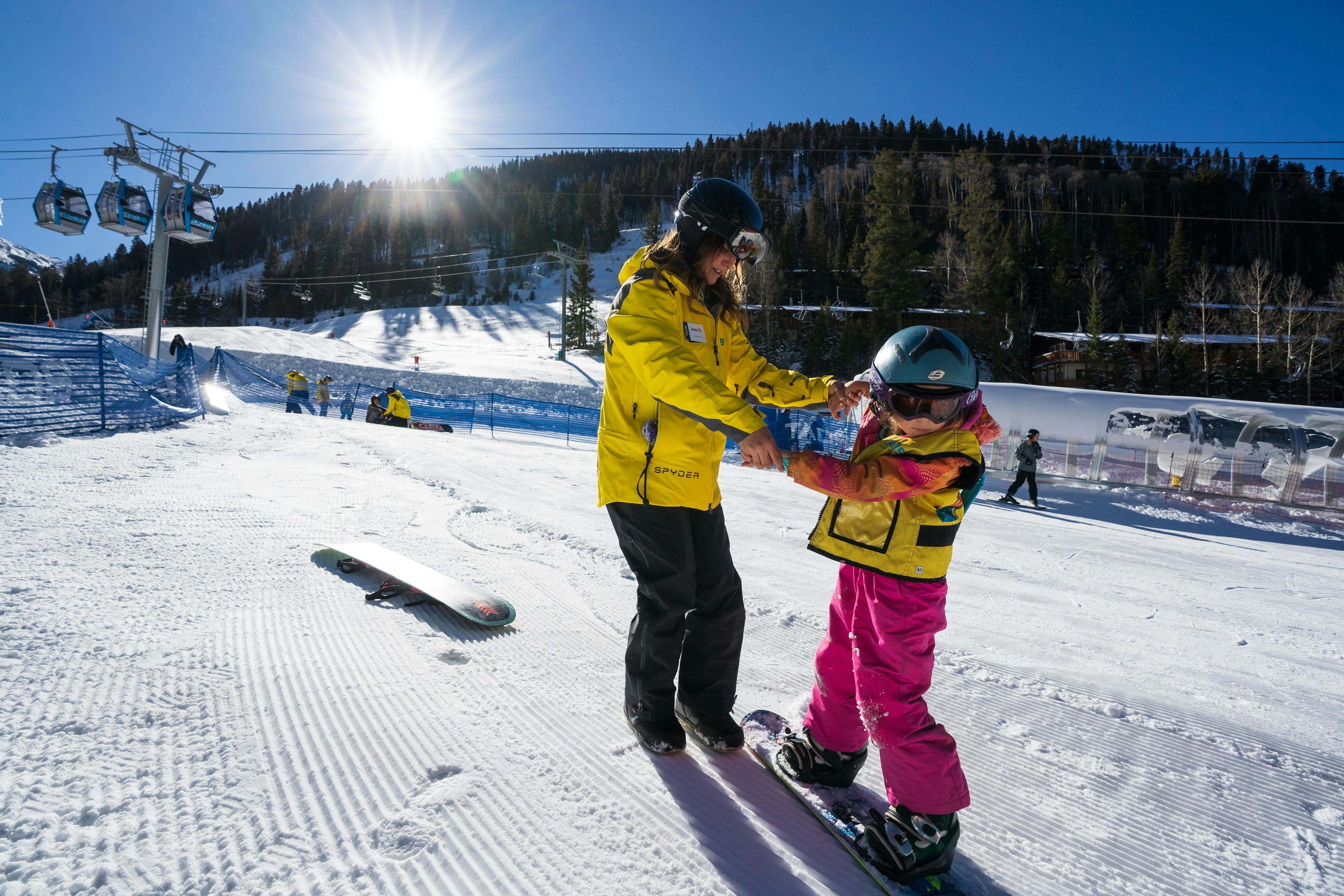 Instructor helping a child learn how to snowboard at Taos Ski Valley.