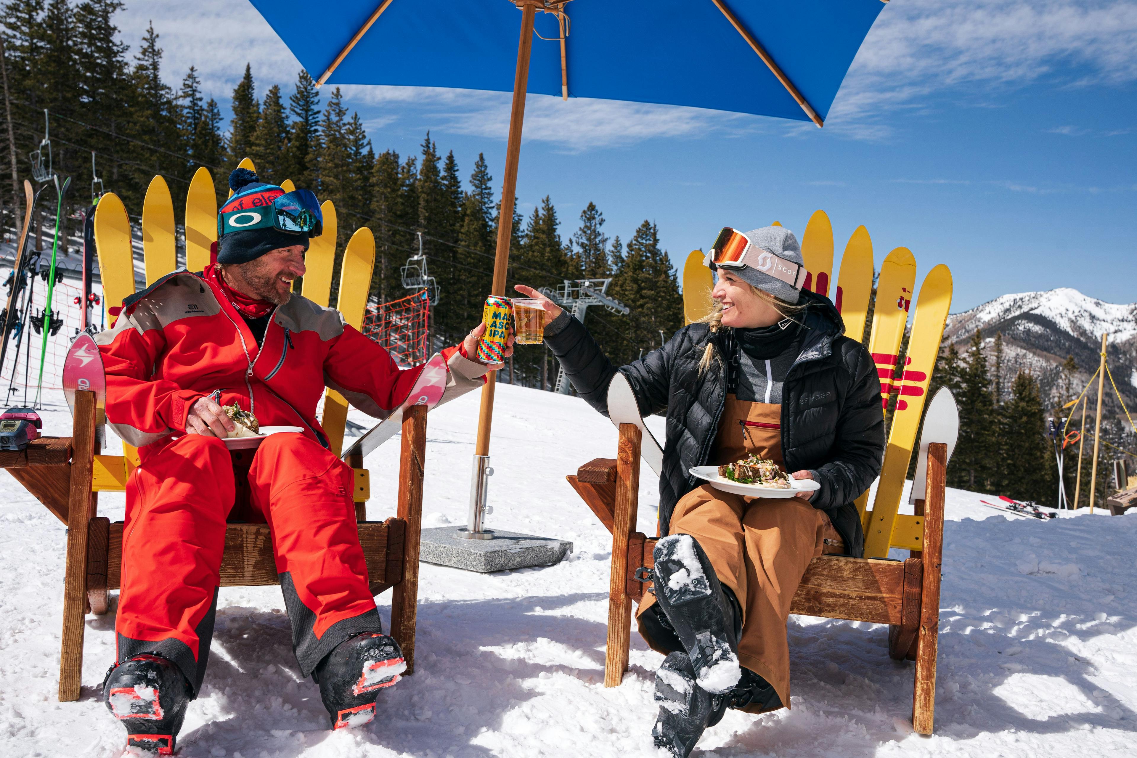 Two skiers cheers their beverages on a sunny day outside the Whistlestop Cafe