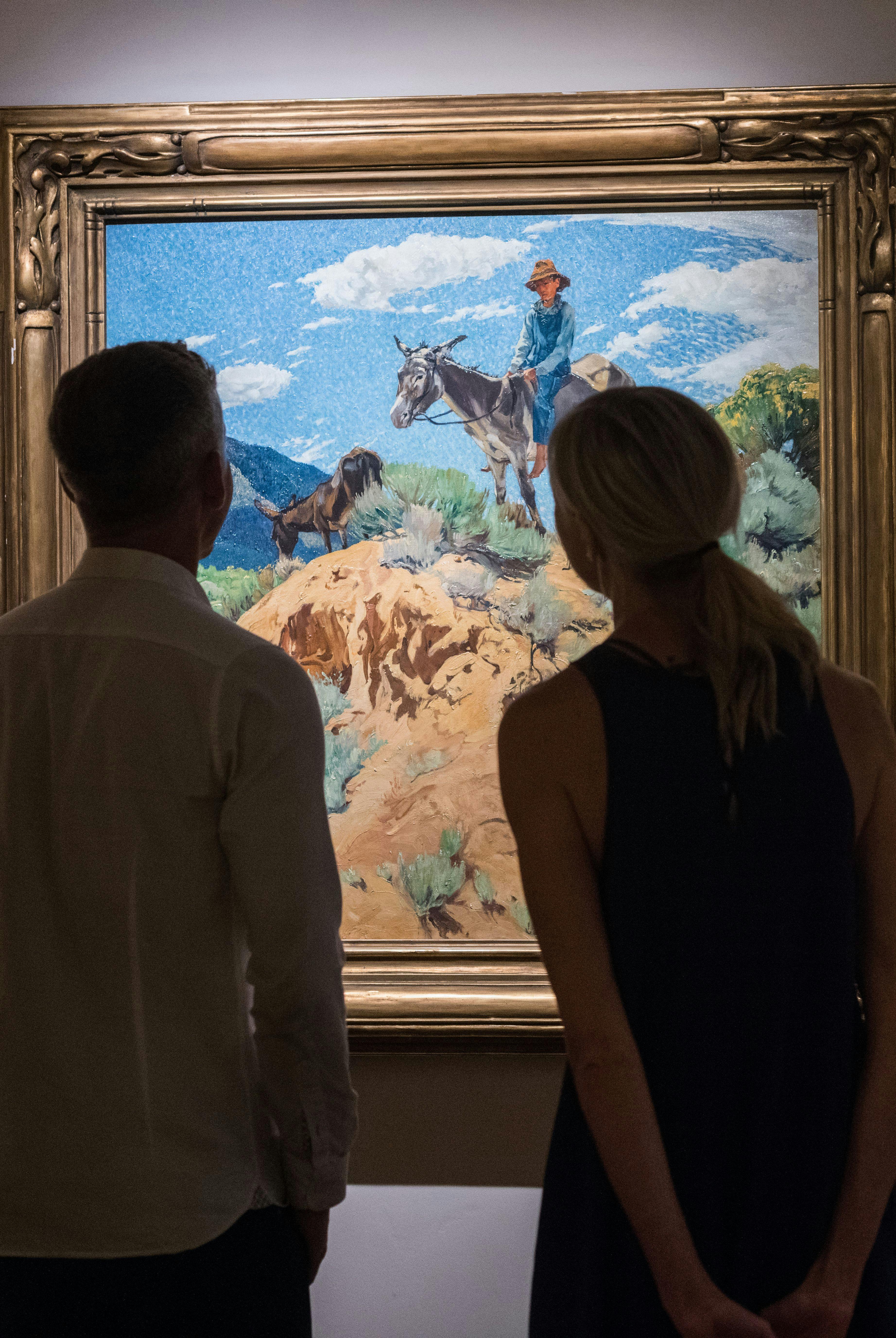 Two guests at The Blake closely observe a painting by a famous Taos artist